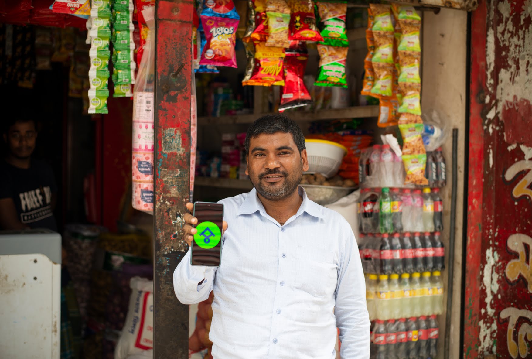 With a phone in his hand, a man is standing in front of a Bangladeshi grocery store. Promoting ShopUp.